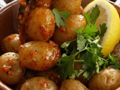 A rustic bowl filled with steaming Cajun garlic butter red potatoes garnished with fresh parsley and lemon.