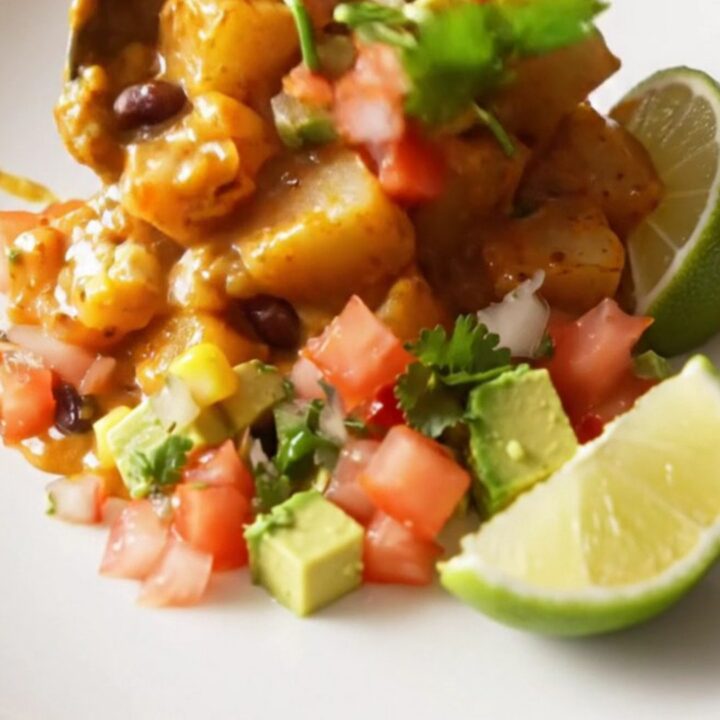 A steaming scoop of smoky chipotle cheddar fiesta potatoes topped with fresh cilantro and avocado in a rustic bowl.