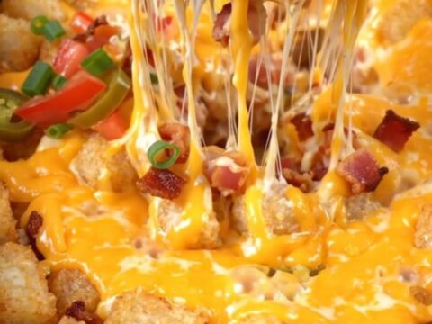 A close-up shot of a loaded tater tot casserole being lifted from a red Crockpot with melted cheese stretching.