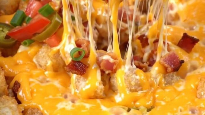 A close-up shot of a loaded tater tot casserole being lifted from a red Crockpot with melted cheese stretching.