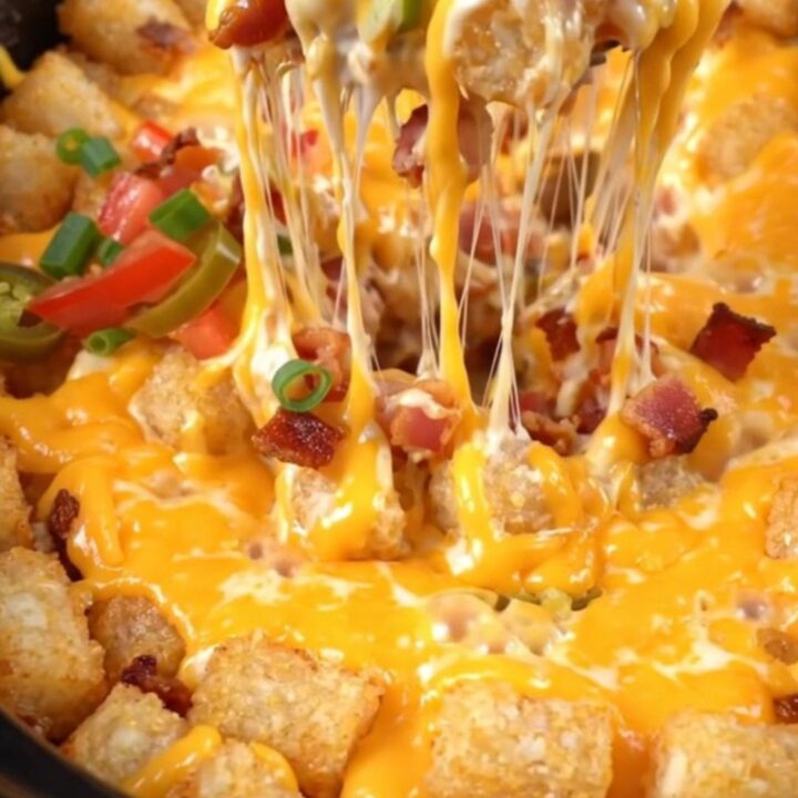 A close-up shot of a loaded tater tot casserole being lifted from a red Crockpot with melted cheese stretching.