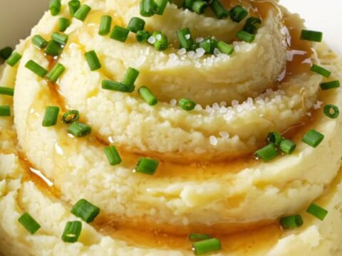 A close-up of creamy mashed potatoes in a bowl, topped with browned butter, fresh chives, and sea salt.