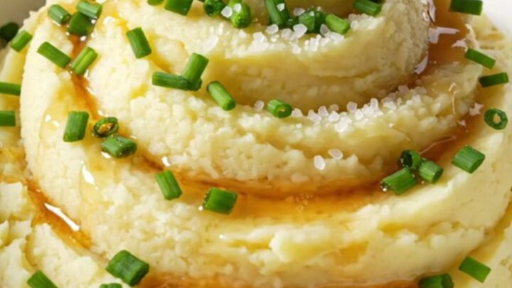 A close-up of creamy mashed potatoes in a bowl, topped with browned butter, fresh chives, and sea salt.
