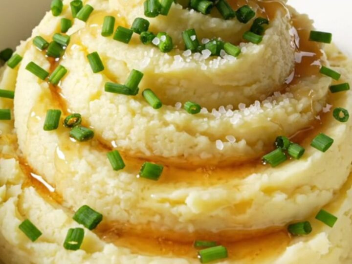 A close-up of creamy mashed potatoes in a bowl, topped with browned butter, fresh chives, and sea salt.