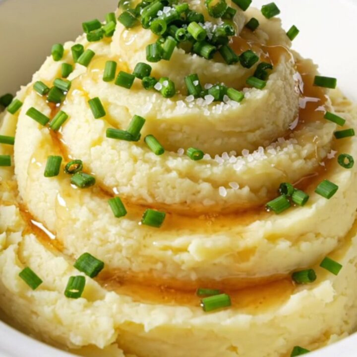 A close-up of creamy mashed potatoes in a bowl, topped with browned butter, fresh chives, and sea salt.