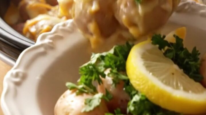 A close-up of tender baby red potatoes coated in a rich, cheesy Old Bay butter sauce inside a golden slow cooker.
