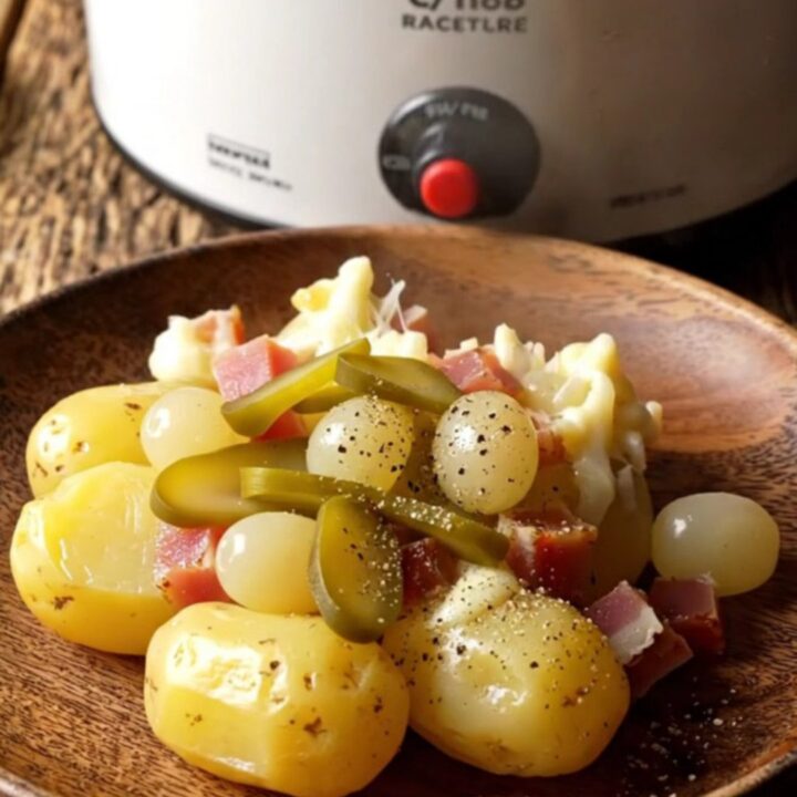 A rustic slow cooker filled with tender baby potatoes, smoky ham, and a thick, bubbly blanket of melted Raclette cheese.