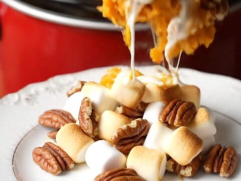A close-up of a crockpot filled with creamy sweet potato casserole topped with toasted marshmallows and pecans.