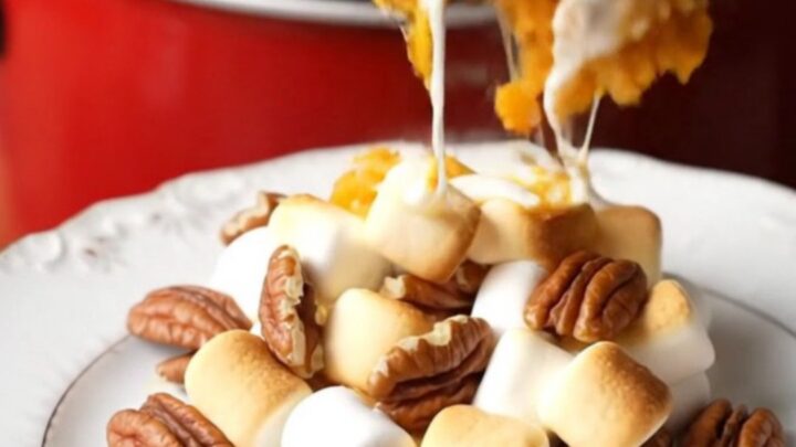 A close-up of a crockpot filled with creamy sweet potato casserole topped with toasted marshmallows and pecans.