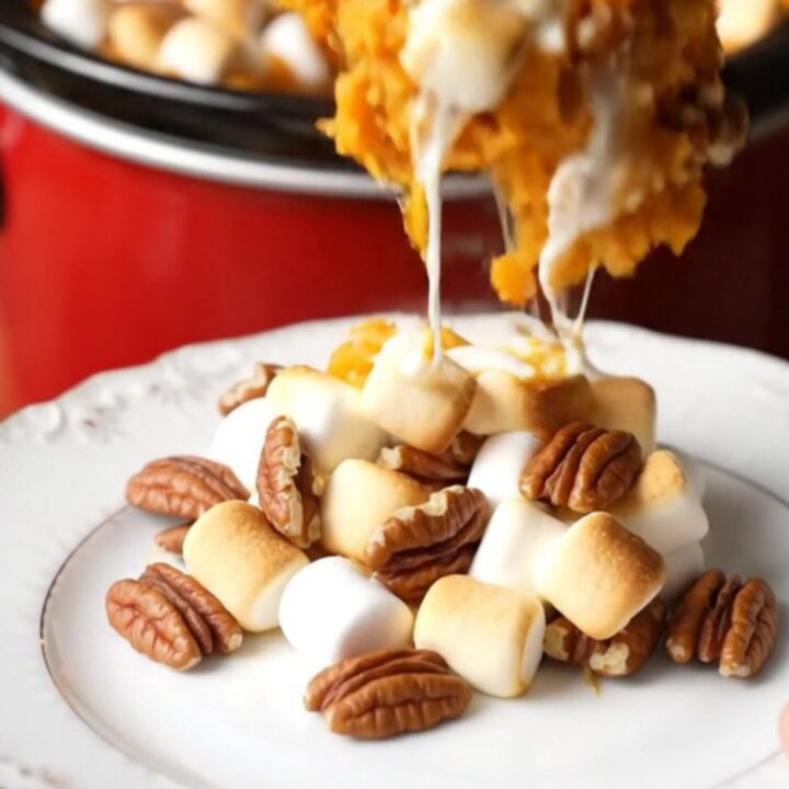 A close-up of a crockpot filled with creamy sweet potato casserole topped with toasted marshmallows and pecans.