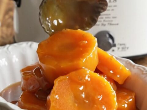 A close-up of tender, caramelized garnet yam medallions in a vintage ceramic slow cooker with bubbling brown sugar syrup.