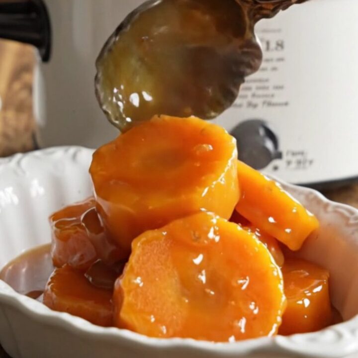 A close-up of tender, caramelized garnet yam medallions in a vintage ceramic slow cooker with bubbling brown sugar syrup.