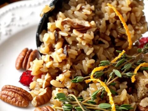 A festive scoop of cranberry pecan wild rice stuffing garnished with fresh thyme in a ceramic bowl.