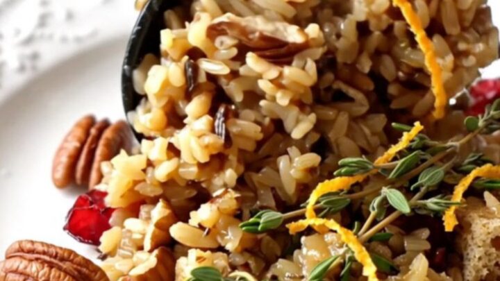 A festive scoop of cranberry pecan wild rice stuffing garnished with fresh thyme in a ceramic bowl.