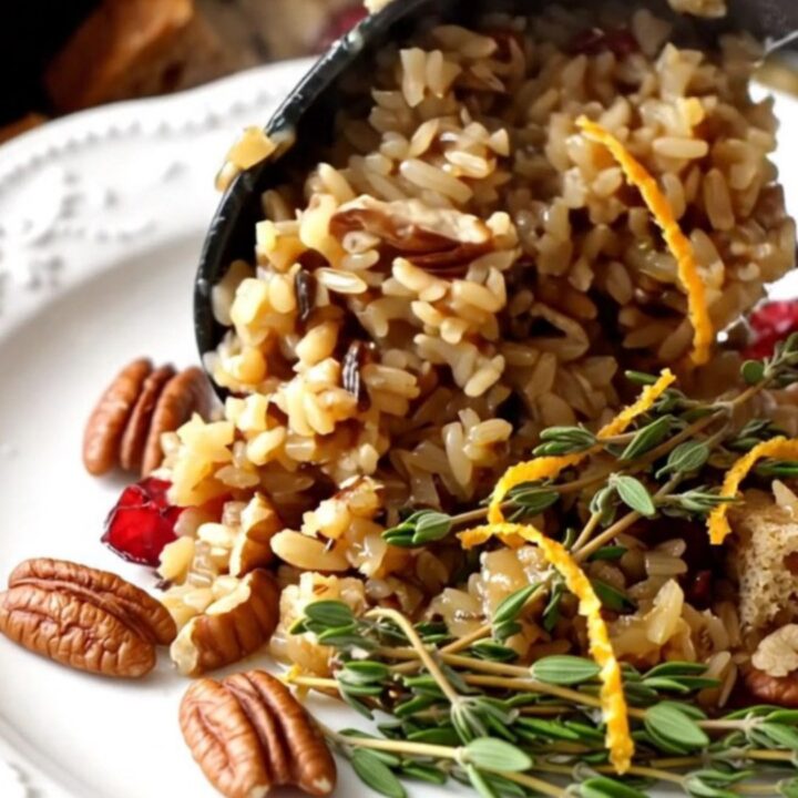 A festive scoop of cranberry pecan wild rice stuffing garnished with fresh thyme in a ceramic bowl.