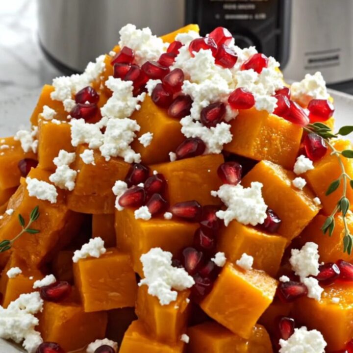 A close-up shot of golden, caramelized butternut squash cubes in a slow cooker, garnished with feta and pomegranate.