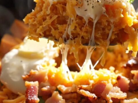 A rustic ceramic slow cooker filled with creamy mashed sweet potatoes topped with melted white cheddar, smoky bacon