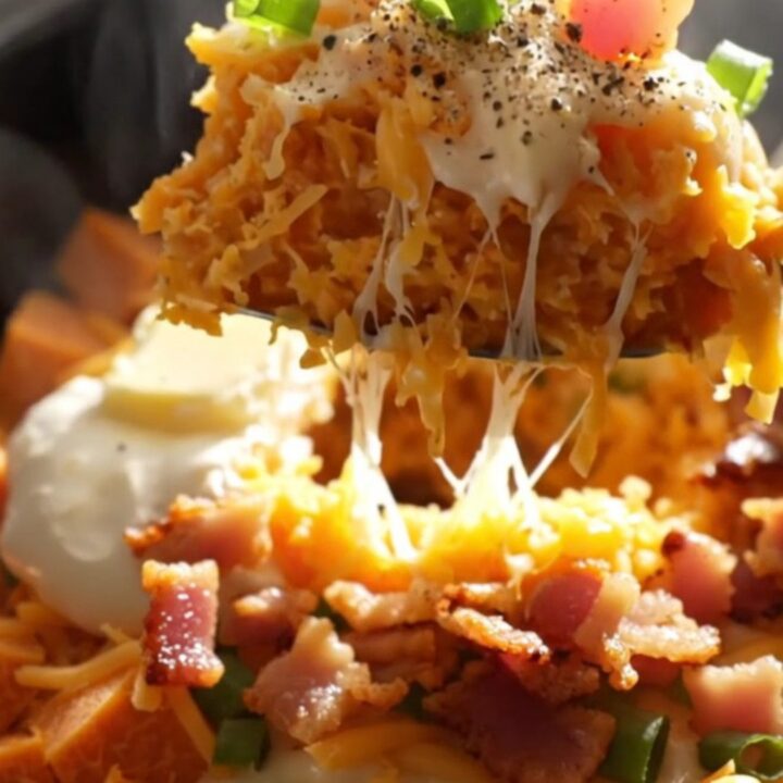 A rustic ceramic slow cooker filled with creamy mashed sweet potatoes topped with melted white cheddar, smoky bacon