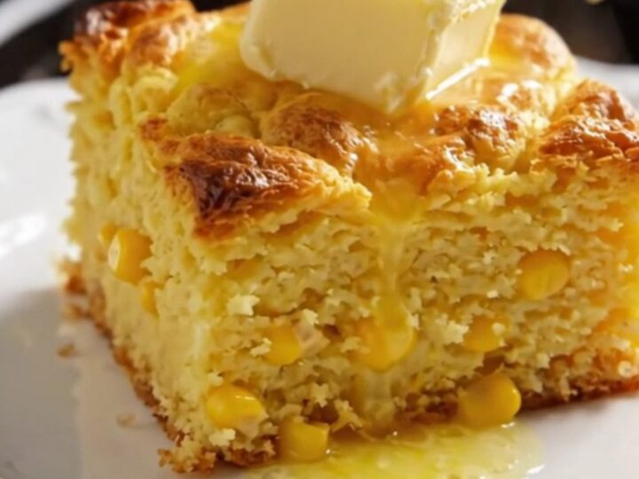 A close-up of a golden, spoon-tender corn casserole in a ceramic slow cooker with a pat of butter melting on top.