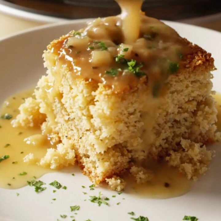 A close-up of a generous scoop of golden, moist Southern cornbread dressing in a cream stoneware Crockpot.