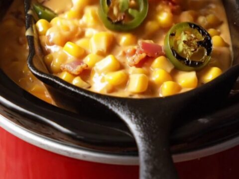 A close-up view of thick, bubbling jalapeño bacon creamed corn in a rustic ceramic slow cooker.