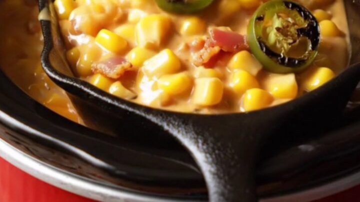 A close-up view of thick, bubbling jalapeño bacon creamed corn in a rustic ceramic slow cooker.