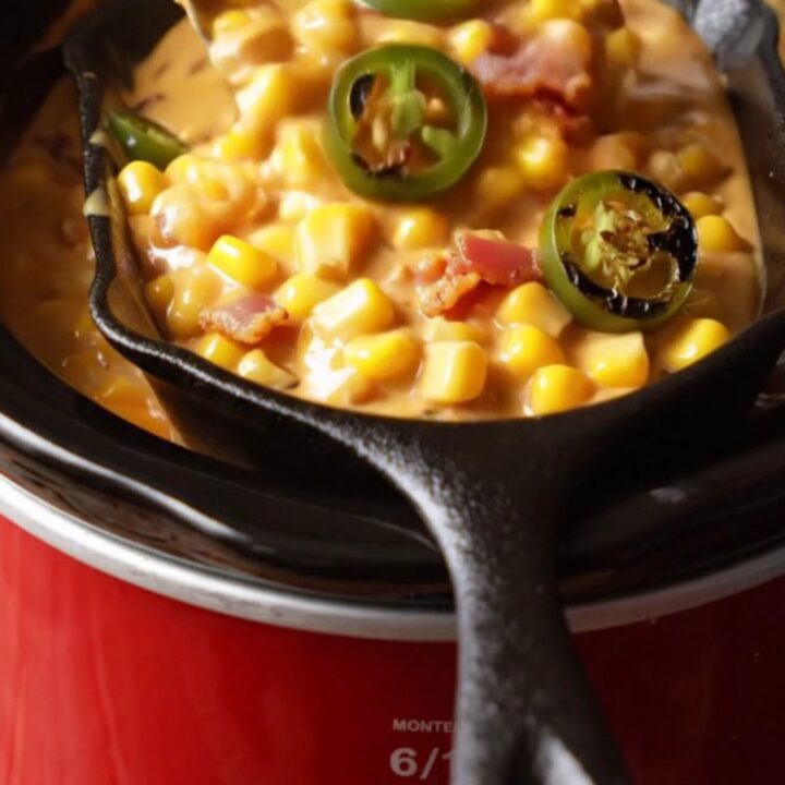 A close-up view of thick, bubbling jalapeño bacon creamed corn in a rustic ceramic slow cooker.