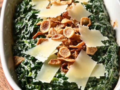A close-up of rich, creamy steakhouse spinach in a black ceramic slow cooker with melted cheese.