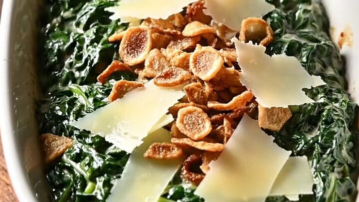 A close-up of rich, creamy steakhouse spinach in a black ceramic slow cooker with melted cheese.