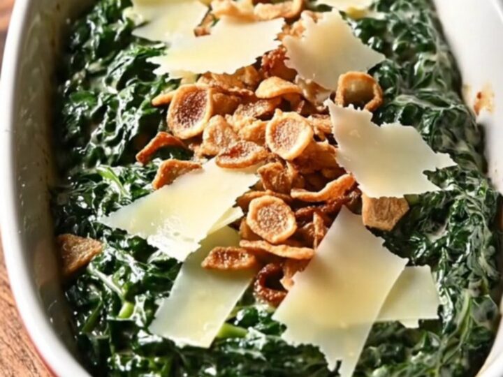 A close-up of rich, creamy steakhouse spinach in a black ceramic slow cooker with melted cheese.