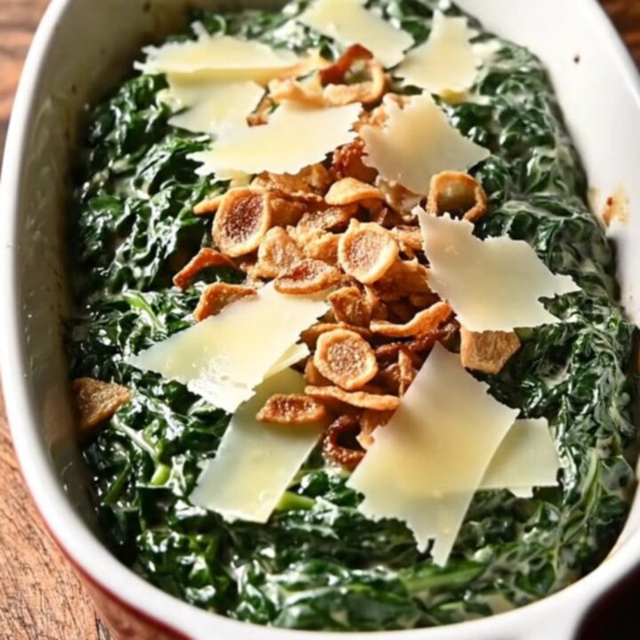 A close-up of rich, creamy steakhouse spinach in a black ceramic slow cooker with melted cheese.