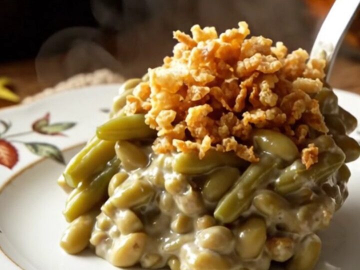A creamy, steaming green bean casserole in a white ceramic slow cooker topped with crispy golden fried onions.