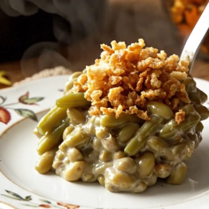 A creamy, steaming green bean casserole in a white ceramic slow cooker topped with crispy golden fried onions.