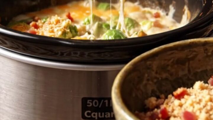 A close-up of a ceramic slow cooker filled with creamy Brussels sprouts au gratin, topped with crispy bacon and breadcrumbs.