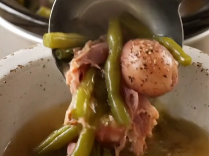 A rustic stoneware bowl filled with tender green beans, baby red potatoes, and shredded smoked ham in a savory broth.