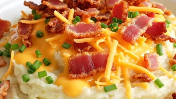 A close-up of a ceramic slow cooker filled with creamy, whipped cauliflower mash topped with melted cheddar, bacon