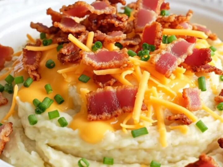A close-up of a ceramic slow cooker filled with creamy, whipped cauliflower mash topped with melted cheddar, bacon