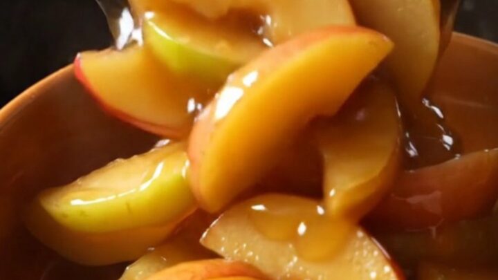 A glass bowl filled with tender, cinnamon-glazed fried apple slices in a rich, golden caramel sauce.