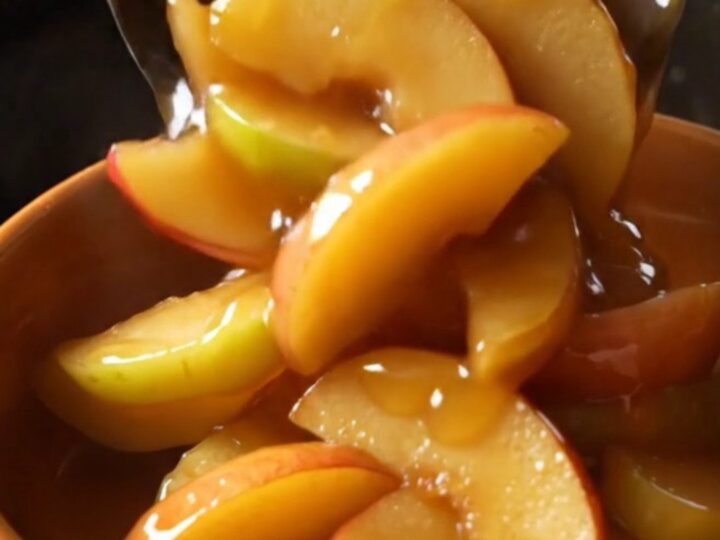 A glass bowl filled with tender, cinnamon-glazed fried apple slices in a rich, golden caramel sauce.
