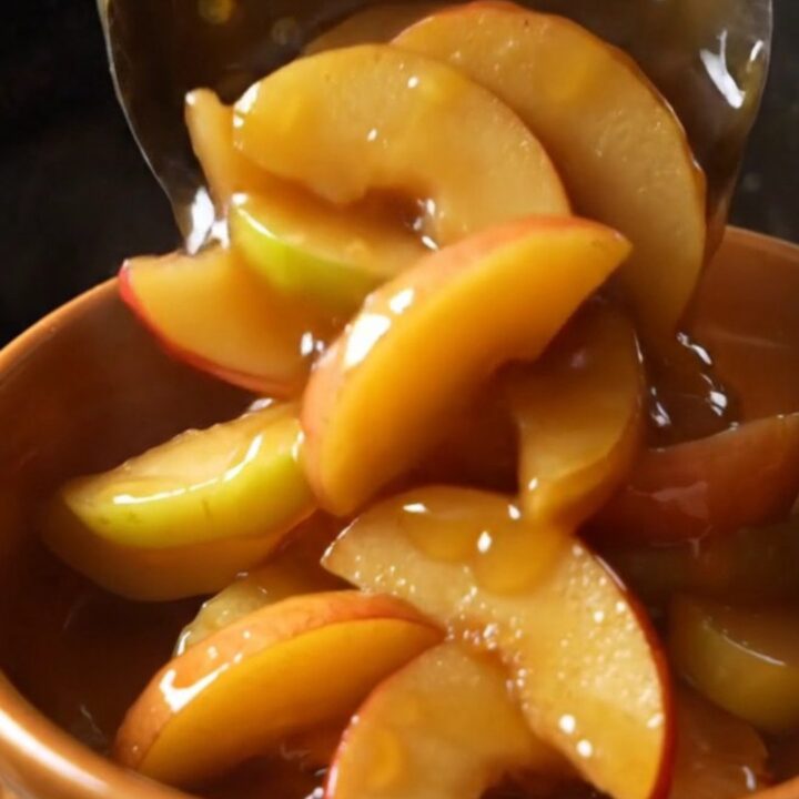 A glass bowl filled with tender, cinnamon-glazed fried apple slices in a rich, golden caramel sauce.