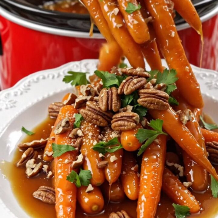A white platter filled with glossy, amber-glazed baby carrots topped with toasted pecans and fresh parsley.
