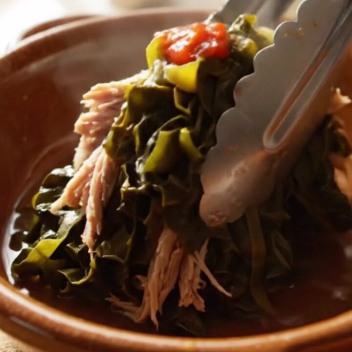 A close-up view of silky, slow-cooked collard greens with shredded smoked turkey in a cream stoneware crockpot.