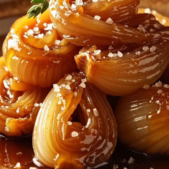 A warm platter of glossy, mahogany-glazed cipollini onions garnished with fresh thyme sprigs.