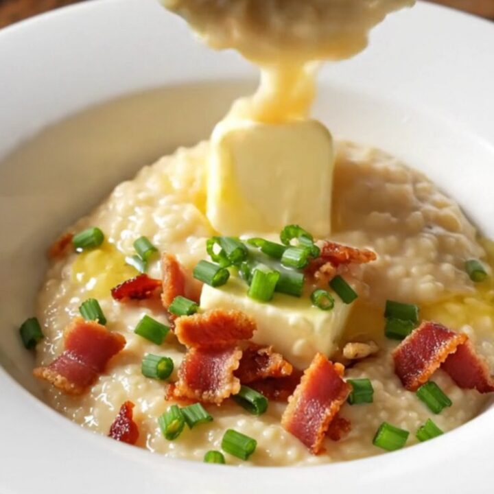 A close-up of creamy, thick cheddar grits served in a bowl, topped with melting butter, crispy bacon, and fresh chives.