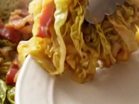 A close-up of tender, buttery braised green cabbage in a red ceramic slow cooker.