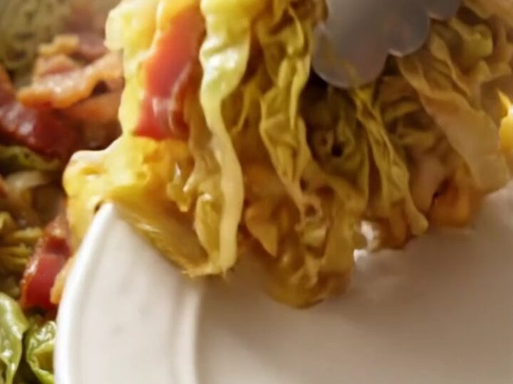 A close-up of tender, buttery braised green cabbage in a red ceramic slow cooker.