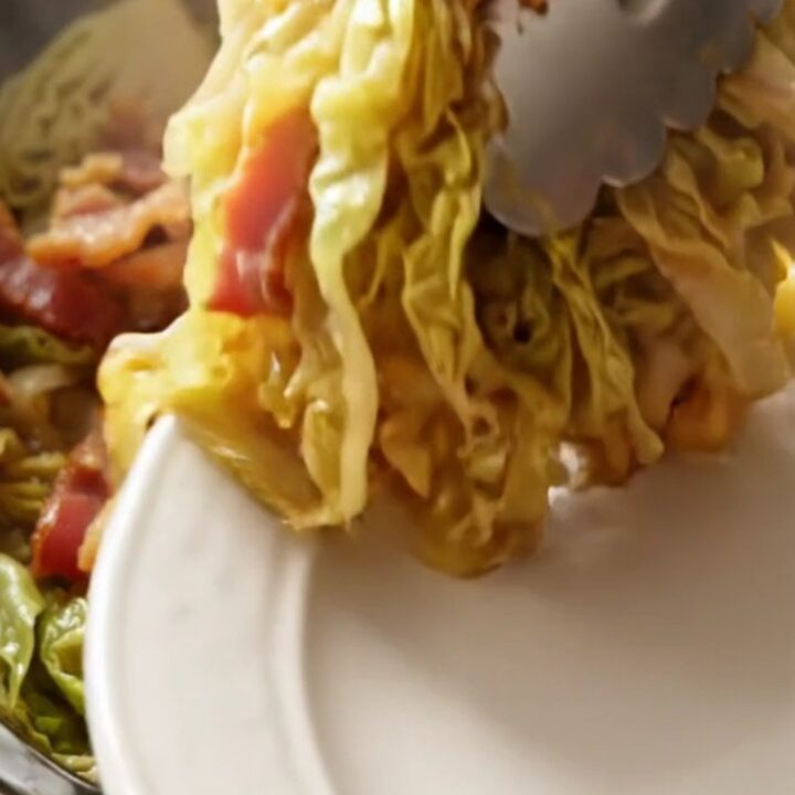 A close-up of tender, buttery braised green cabbage in a red ceramic slow cooker.