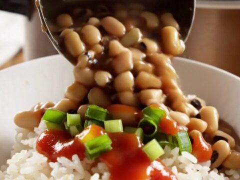 A close-up shot of a dark bronze slow cooker filled with creamy black-eyed peas, smoky ham, and vegetables.
