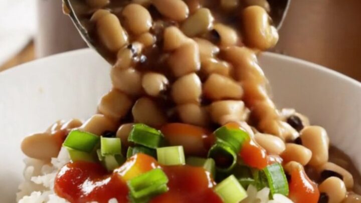 A close-up shot of a dark bronze slow cooker filled with creamy black-eyed peas, smoky ham, and vegetables.