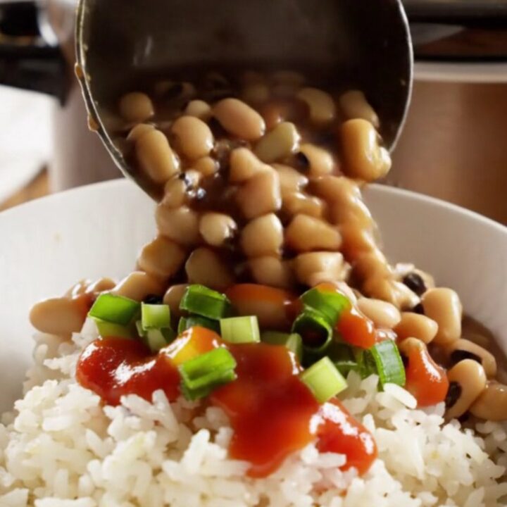 A close-up shot of a dark bronze slow cooker filled with creamy black-eyed peas, smoky ham, and vegetables.